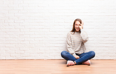 young blonde pretty girl smiling happily with funny face, joking and looking through peephole,...