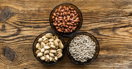 Obraz na płótnie Canvas Sunflower seeds, pistachios and peanuts in a small plates which standing on a wooden vintage table. Nuts is a healthy vegetarian protein and nutritious food. Nuts on rustic old wood.