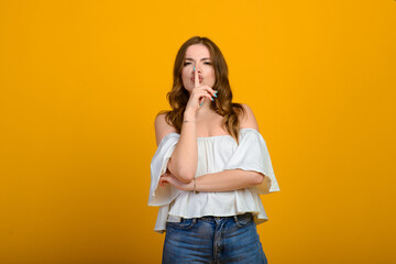 Dark-haired young woman with a smile and big suprised eyes posing on yellow background.