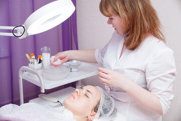 Beautician washes woman's face using cotton pads.