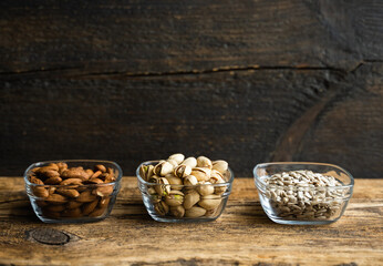 Almond, pistachio and sunflower seeds in a small plates which standing on a wooden vintage table. Nuts is a healthy vegetarian protein and nutritious food. Nuts on rustic old wood.