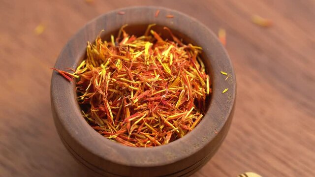 Saffron spice threads in bowl on wooden background rotation