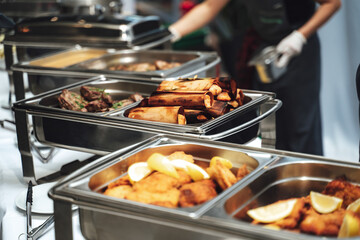 Row of stainless hotel pans on food warmers with various meals. Self-service buffet table....