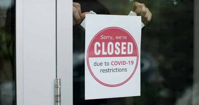 Closed due to Covid sign. Business owner places sign on the storefront. Storefront sign of closure due to covid -19 placed on the door. Small business closing down. Shot in slow-motion in 4k on RED ca