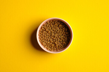 Bowl of dry kibble cat food on yellow background top view. Pet care concept.