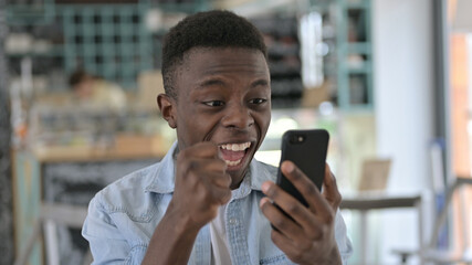 Fototapeta premium Portrait of Young African Man Celebrating Success on Smartphone