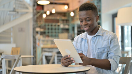 Cheerful Young African Man Using Tablet in Cafe