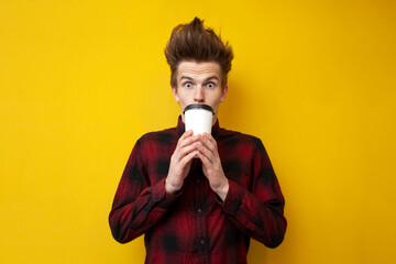 shocked guy drinks invigorating coffee and is surprised at a yellow isolated background, a man...