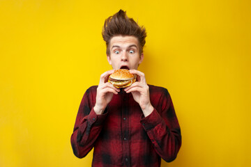shocked guy eating a burger on a yellow isolated background, hipster with funny hairstyle holds...