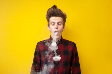 guy vaper does tricks with smoke on a yellow isolated background, man exhales smoke rings