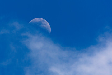 Obraz na płótnie Canvas Moon in broad daylight, half hidden behind a cloud