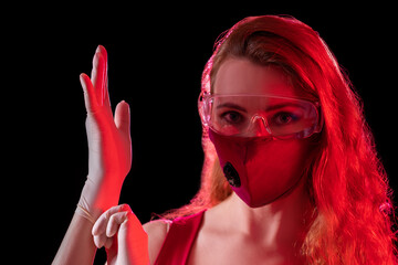 Woman wearing protective glasses and a safety mask. On her hands she has gloves.  Red contract dramatic colors. 