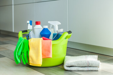 A set of cleaning products on the floor in a basin, next to a rag for the floor.