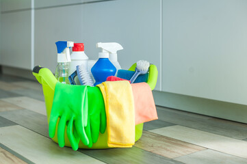 A set of cleaning products on the floor in a basin, rags, brushes, gloves and various cleaning products for the apartment.