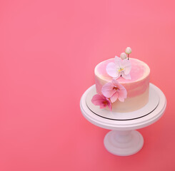 Pink cake stands on a round white stand on a pink background. Cake decorated with sugar flowers orchids. Beautiful dessert decorated with flowers.