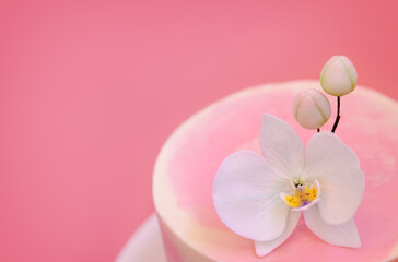 Fototapeta na wymiar Cake decorated with sugar flower orchid close-up top view. Pink marble cake stands on a round white stand on a pink background. Beautiful dessert decorated with flowers.
