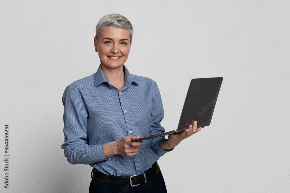 Wall mural mature age employment concept. smiling middle-aged woman posing with laptop in hands