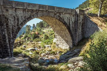Fototapeta na wymiar Small stream passing between stones under a Roman stone bridge overlooking the rural landscape in the Serra da Estrela Natural Park, Loriga PORTUGAL