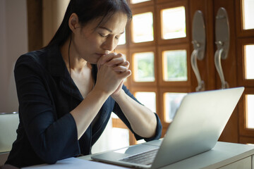 Asian woman praying by faith with laptop, book, notebook on it, praying position. Online church...