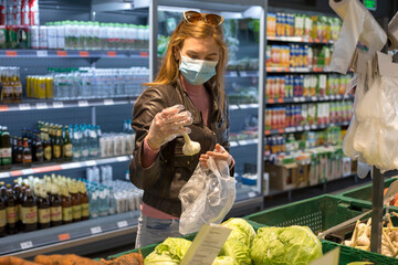 Girl in medical mask and gloves chooses garlic in supermarket. Shopping during pandemic