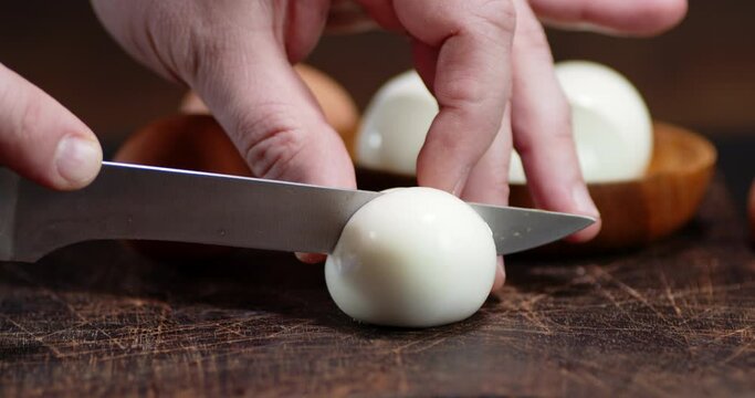 Hand of a man with a knife cut boiled egg into two halves.