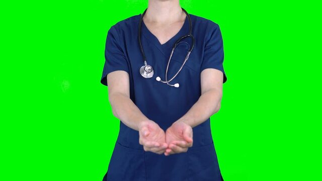 4K female nurse doctor on green screen isolated with chroma key. Woman holding empty space with both hands, offering invisible object in palms. Copy space for text or image. Cropped front view
