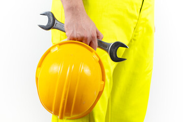 Man in yellow worker overalls holds yellow hard hat and wrench.