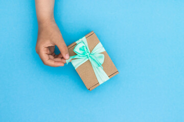 Hands giving or receiving a gift in craft paper with a mint ribbon on blue background. Top view. Copy space.