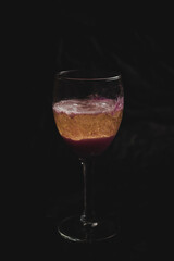 Sparkling wine in a cocktail with red fruit coloring, freshly served in a small glass, the foam and the gas can be perceived perfectly.