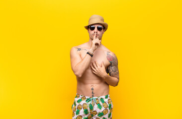 young handsome man looking serious and cross with finger pressed to lips demanding silence or...
