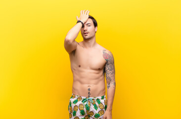 young handsome man raising palm to forehead thinking oops, after making a stupid mistake or...