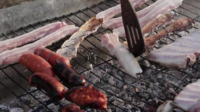 Una mano de un chico cocinando panceta sobre una parrilla r&uacute;stica sobre el fuego 