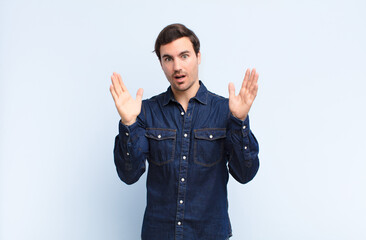 young handsome man looking shocked and astonished, with jaw dropped in surprise when realizing...