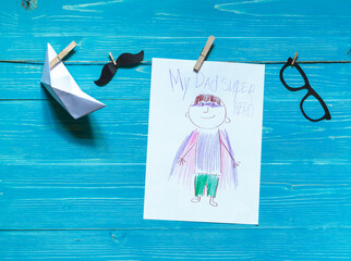 Children's drawing of super hero dad, paper boat, paper mustache and glasses on a string,...