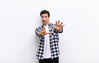 young handsome man feeling terrified, backing off and screaming in horror and panic, reacting to a...