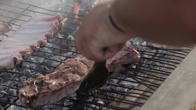 Una mano de chico cocinando costillas sobre una parrilla con fuego debajo