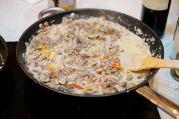 Mushrooms with vegetables are fried in a pan on an induction stove.