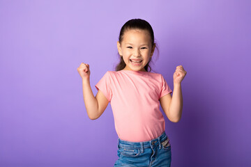 Happy little asian girl shaking fists, making winner gesture