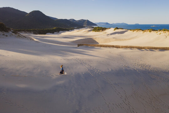 Aerial shot of lonely person isolated walking on the dunes with white sand, beach sea ocean and mountains far away.