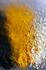 Vertical image of three color explosion of back orange and white - activated carbon, turmeric and coconut on grey background