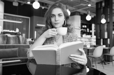 Fototapeta na wymiar Young beautiful woman drinks coffee and reading book in cafe