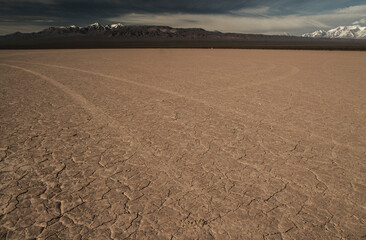 Fototapeta premium Textured ground. Arid desert field landscape with the mountains in the background. Vast clay terrain in dry weather creating texture and pattern.