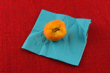 Partially eaten fresh raw apricot with pit on blue napkin on red tablecloth