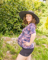 happy pregnant woman in sportswear and black hat outdoors in green park.