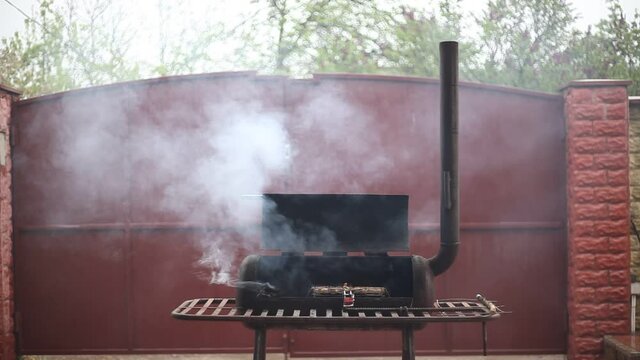 Cooking shashlik in the grill. Smoking juicy meat sausages on the metal grate on the open barbecue. Thick smoke from the mangal. Street food concept.