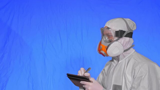 Scientist virologist in respirator makes write in an tablet computer with stylus. Man wearing protective medical mask. Concept health safety virus coronavirus epidemic 2019 nCoV. Chroma key blue.