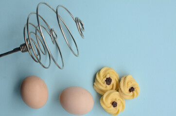 pastry with chicken eggs and manual hand egg beater on a blue background
