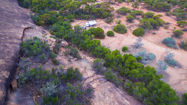 Oblique drone view of a 4WD and a caravan in  at a free camp near a granite outcrop in the Australian outback.