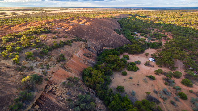 Oblique drone view of a 4WD and a caravan in  at a free camp near a granite outcrop in the Australian outback.
