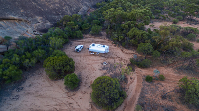 Oblique drone view of a 4WD and a caravan in  at a free camp near a granite outcrop in the Australian outback.